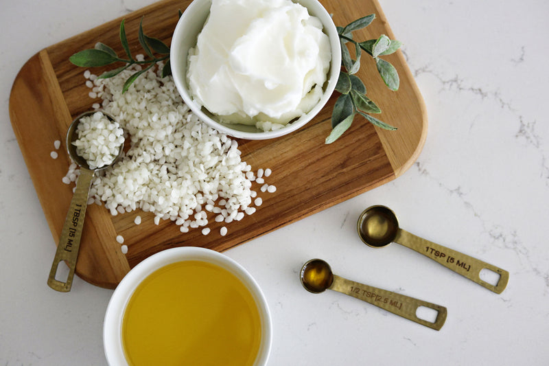 Wooden cutting board with a bowl of liquid, and measuring spoons on a marble surface.
