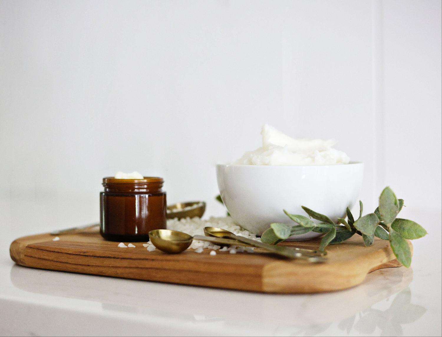 Bowl of white tallow balm on a wooden tray with a jar and small bowl on a light background