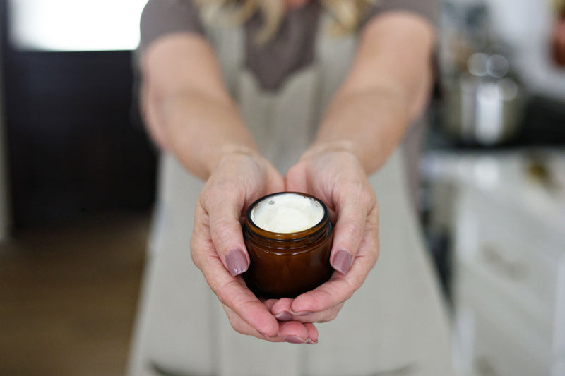 Person holding a small brown jar with a white lid in a kitchen setting