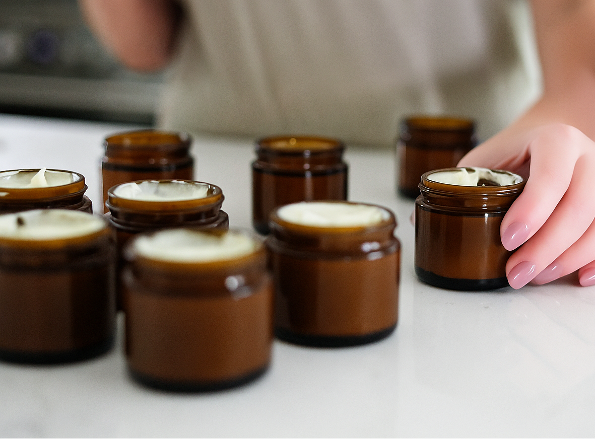 Person arranging small brown jars with white substance on a light surface